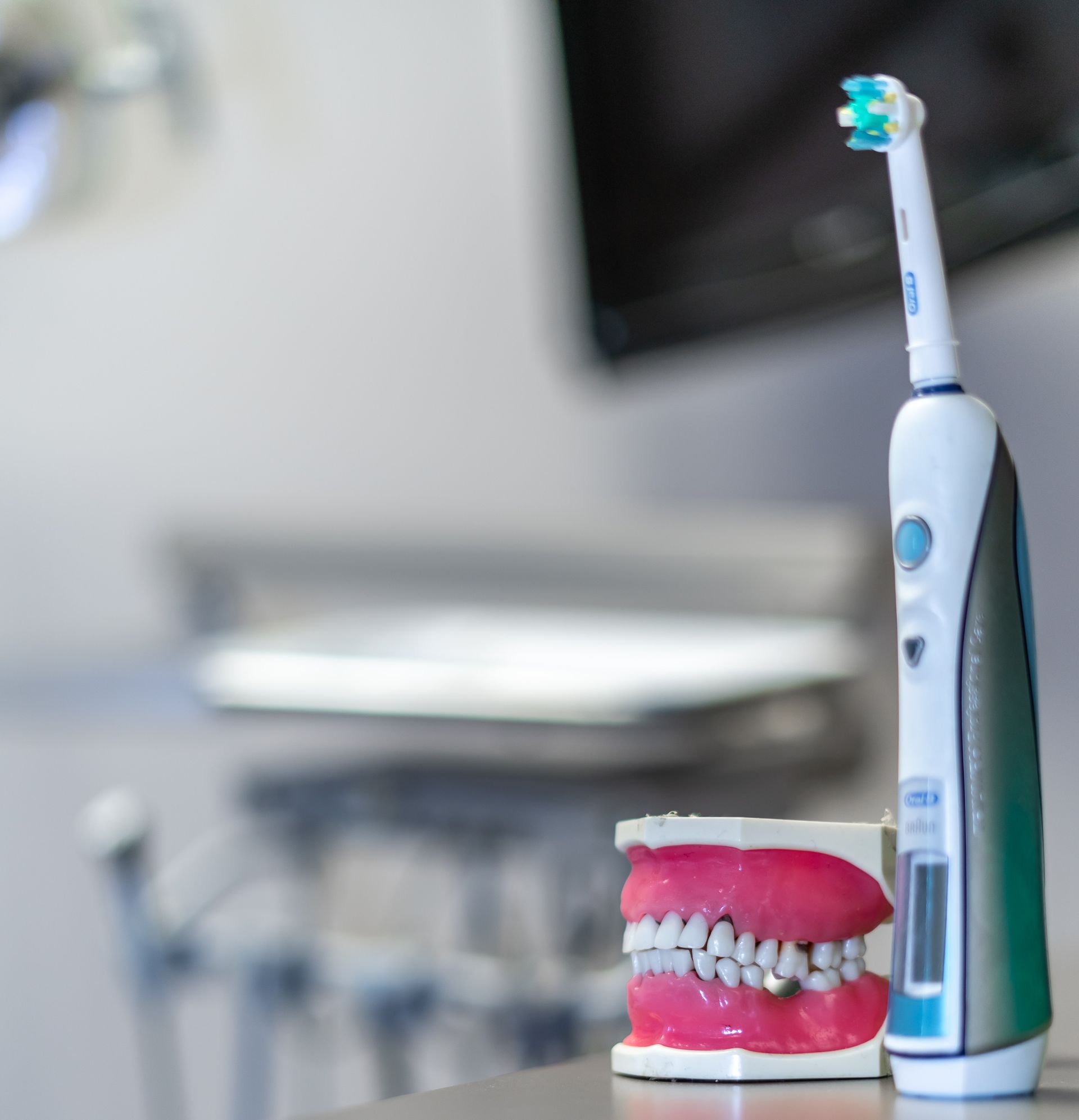 An electric toothbrush is sitting next to a model of teeth
