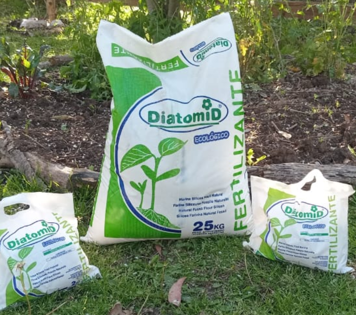 Dos bolsas blancas de fertilizante sobre el césped de un jardín.