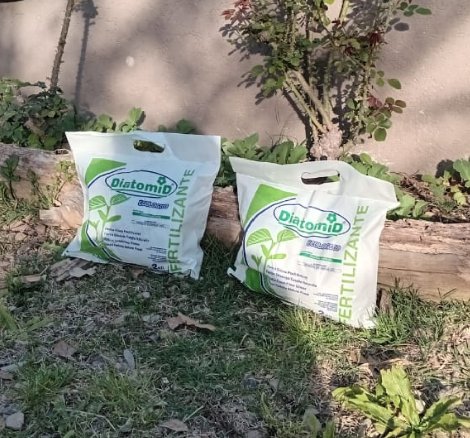 Dos bolsas blancas de fertilizante sobre el césped de un jardín.