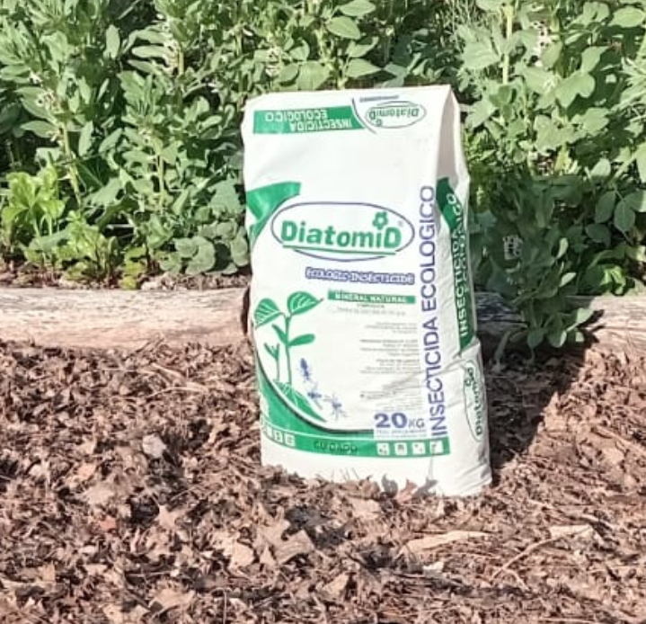 Una bolsa blanca de "Diatomio Insecticida Ecologico" en un cantero con plantas.