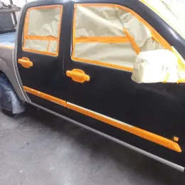 Black truck door being painted with masking tape protecting windows, handles.
