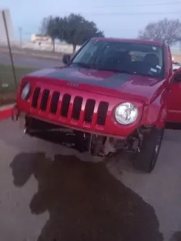 Red Jeep with front-end damage, likely in an accident, parked near a curb. Water puddle visible.