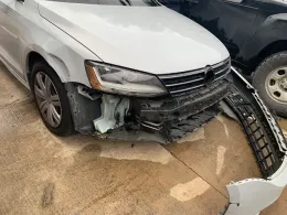 White Volkswagen Jetta with front-end damage, bumper detached, sitting on concrete.