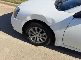 White car with a dented front fender, parked on a concrete surface.