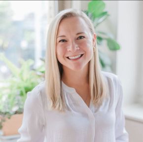 A woman in a white shirt is smiling in front of a window.