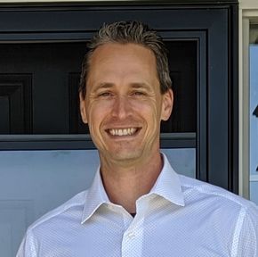 A man in a white shirt is smiling in front of a door.