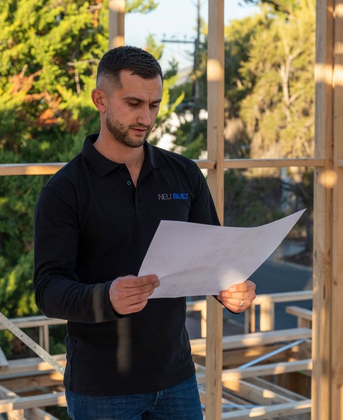 Spero Koulianos of Neu Built wearing a black long-sleeved polo shirt, reading plans.