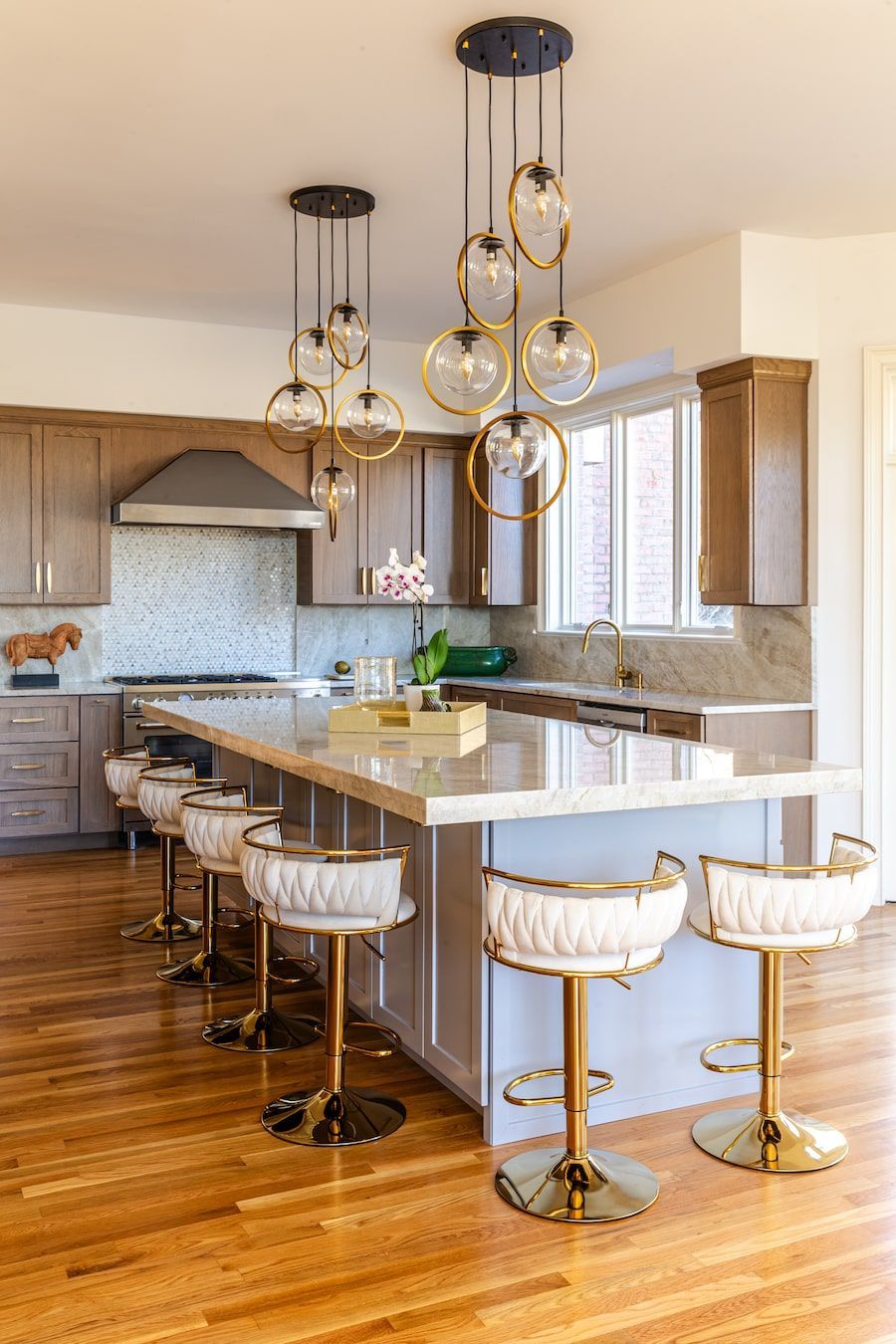 Kitchen with a long island, gold bar stools, pendant lights, and wooden floors.