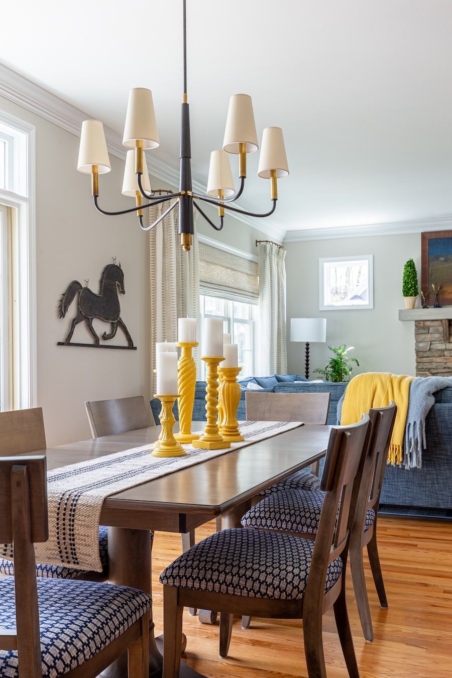 Dining room with wooden table, patterned chairs, yellow candlesticks, and black chandelier.