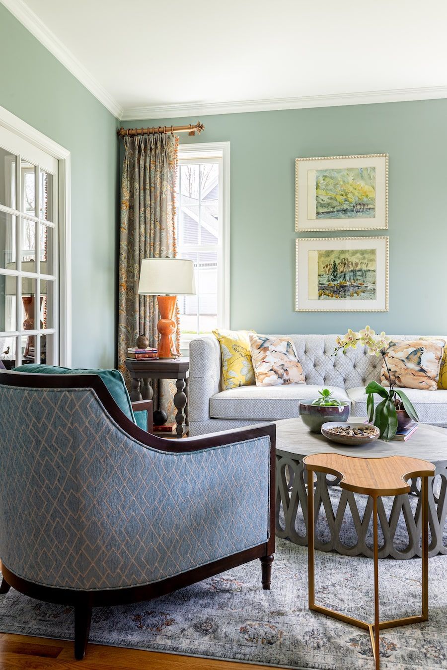 Living room with blue-green walls, gray sofa, patterned chair, and artwork.