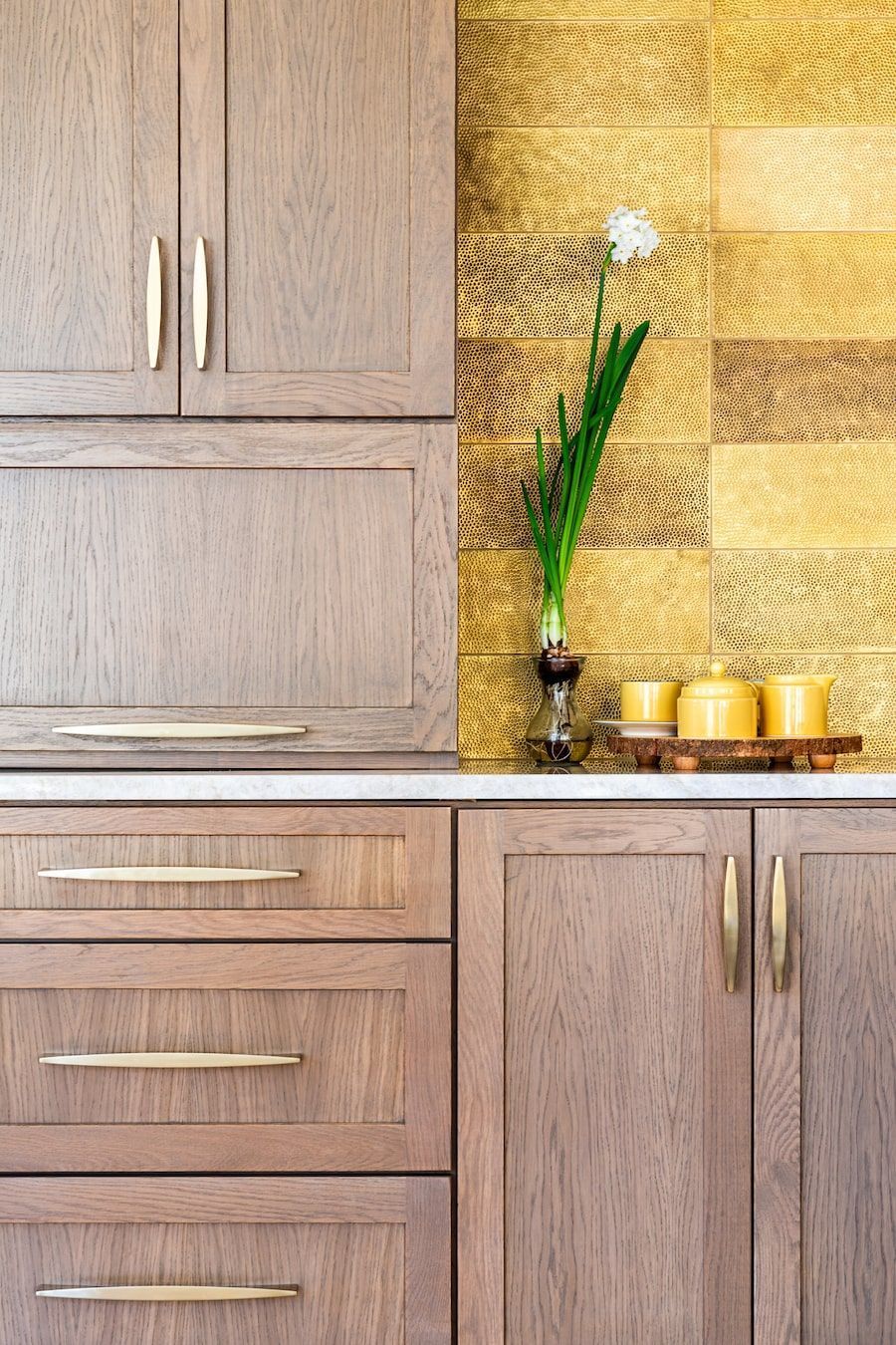 Kitchen cabinetry with a gold backsplash and a flower arrangement.
