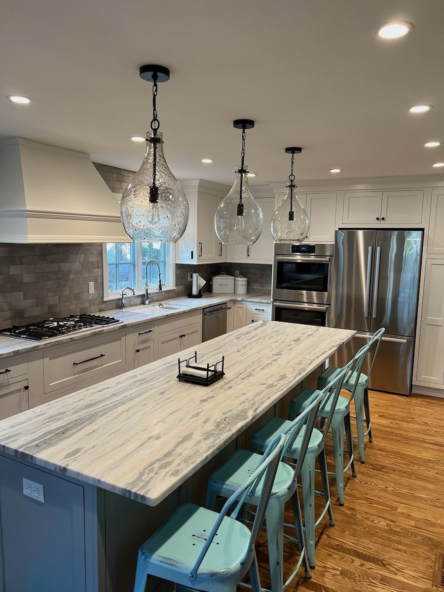 Kitchen with a long island, clear pendant lights, and turquoise stools. Includes stainless steel appliances.