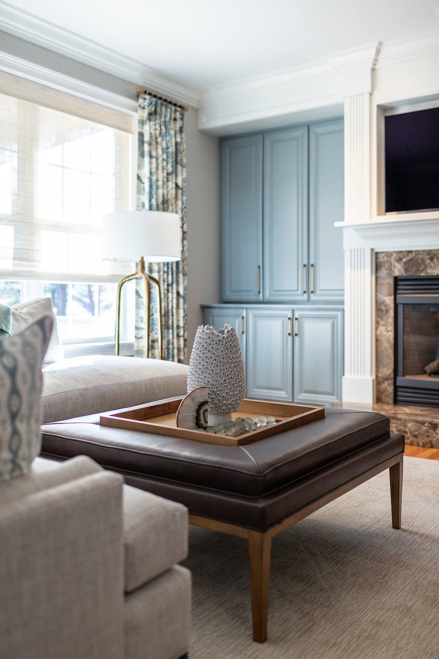 Living room with a brown ottoman, blue cabinets, and a fireplace.