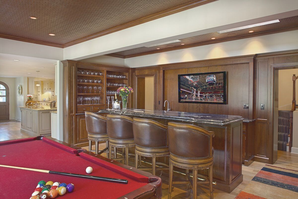 Pool table in a rec room with a bar, brown stools, TV.