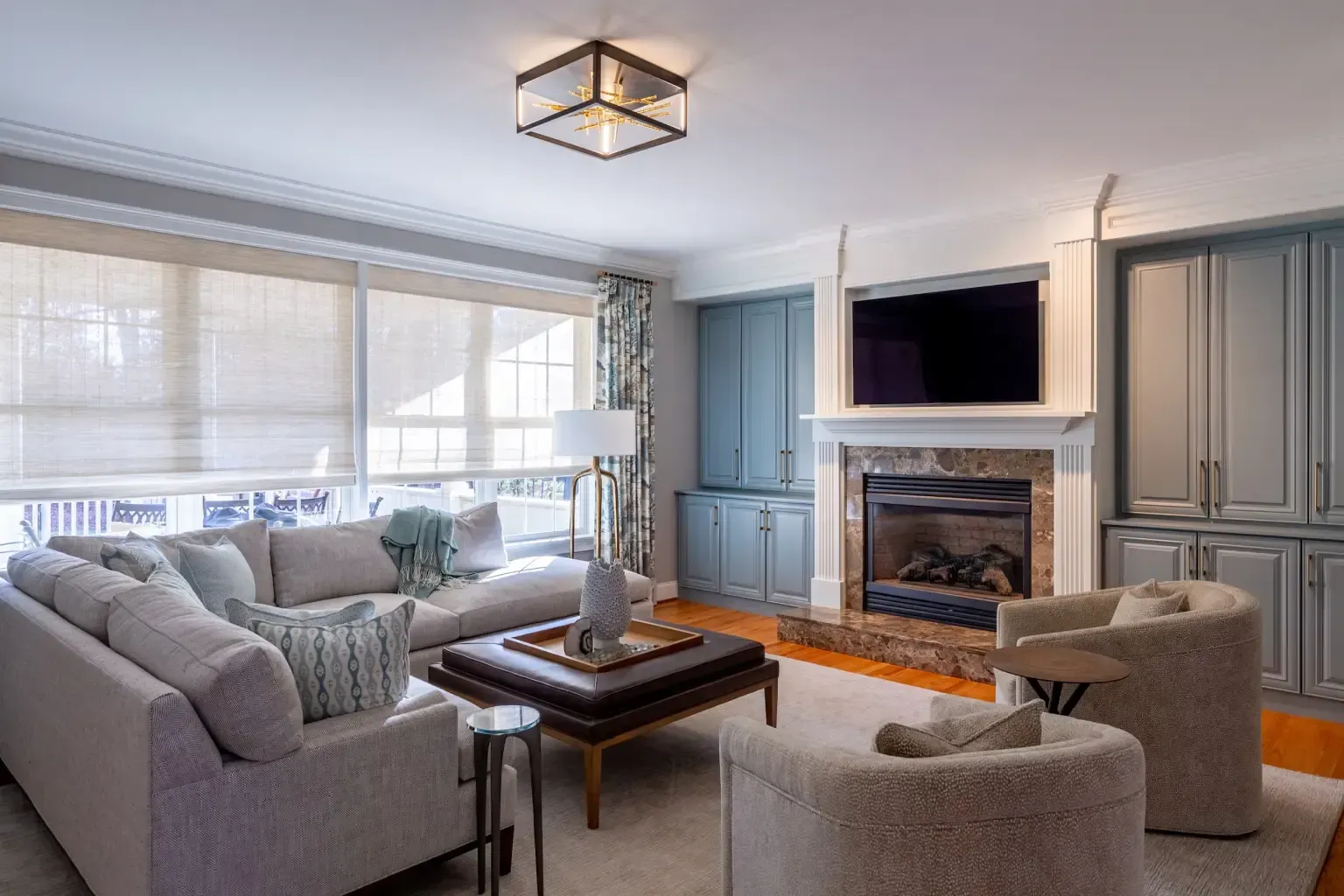 Cozy living room with fireplace, built-ins, large window, light gray sectional, and brown ottoman.