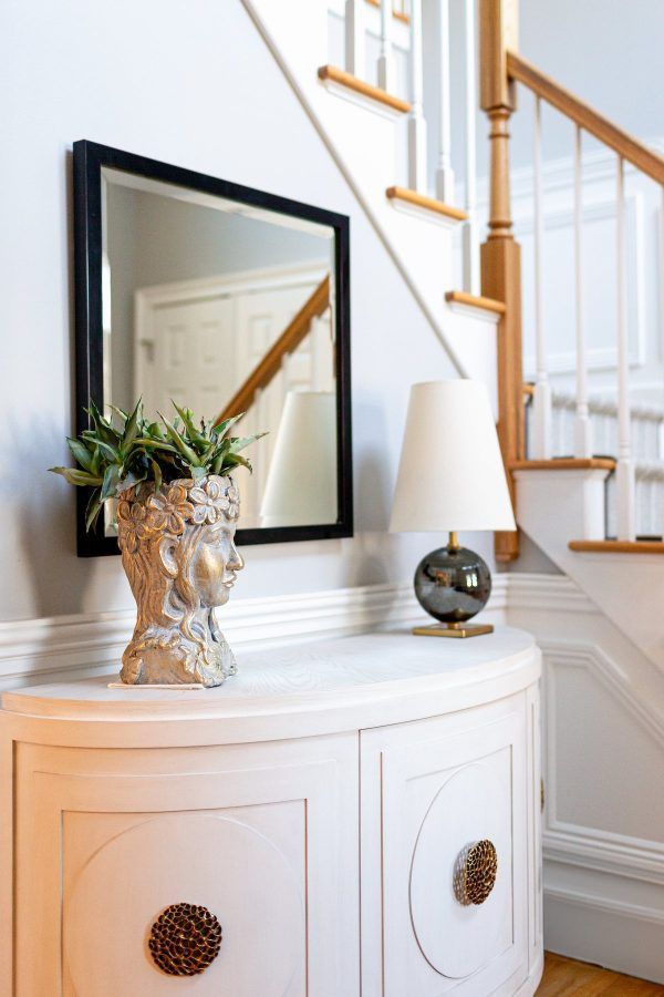 White console table with decor, black mirror, and staircase in a bright entryway.