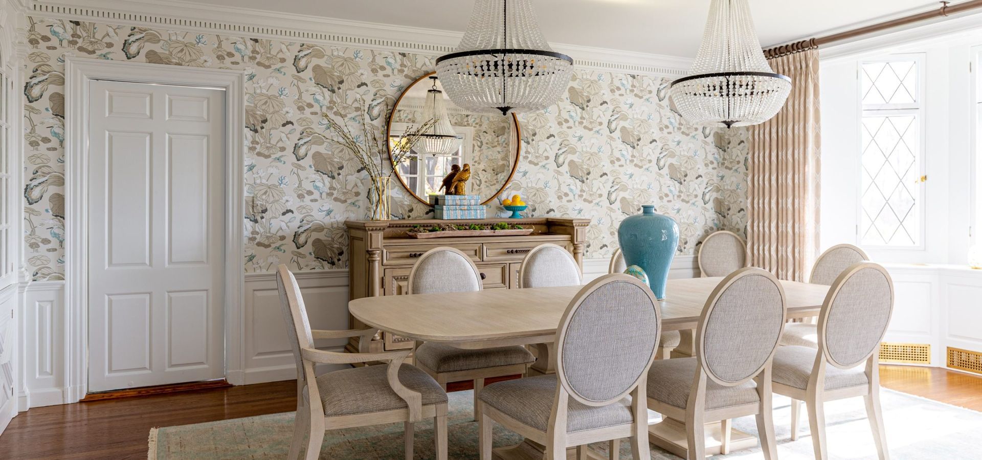 Elegant dining room with floral wallpaper, a wooden table, chairs, and large chandelier.