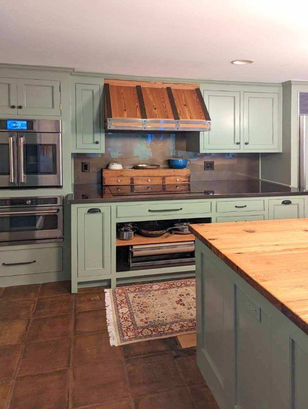Green kitchen with wooden accents; stainless steel appliances.