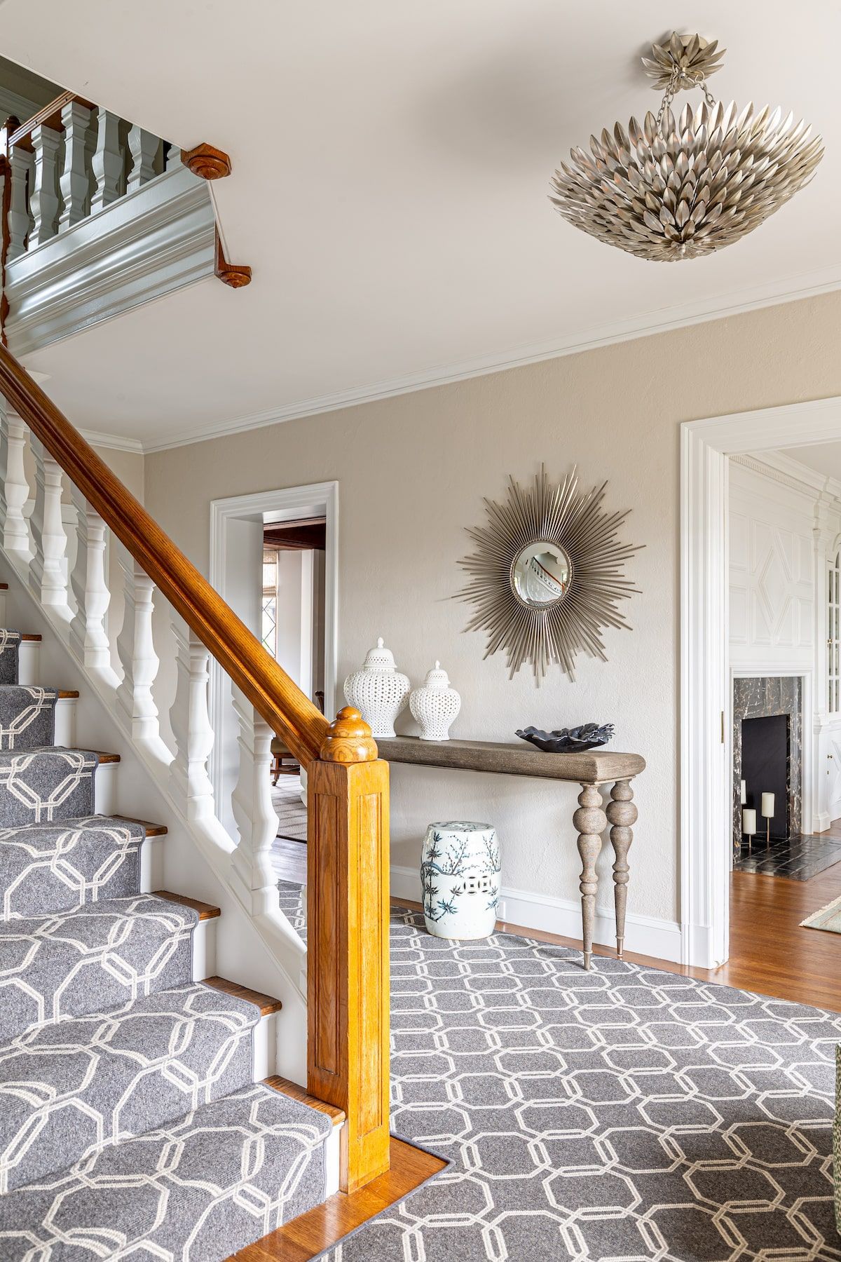 Staircase with patterned carpet, wooden railing, and console table with a sunburst mirror.
