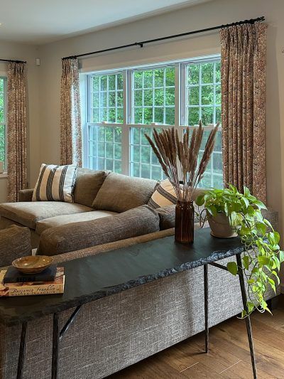 Living room with brown sectional sofa, floral curtains, slate console table, and plants.