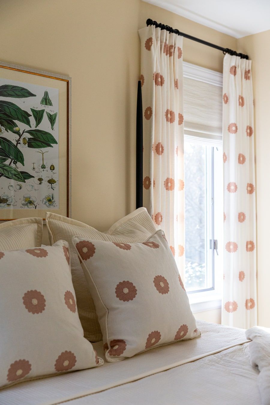 Bedroom with bed, floral pillows and curtains; botanical print artwork on wall.
