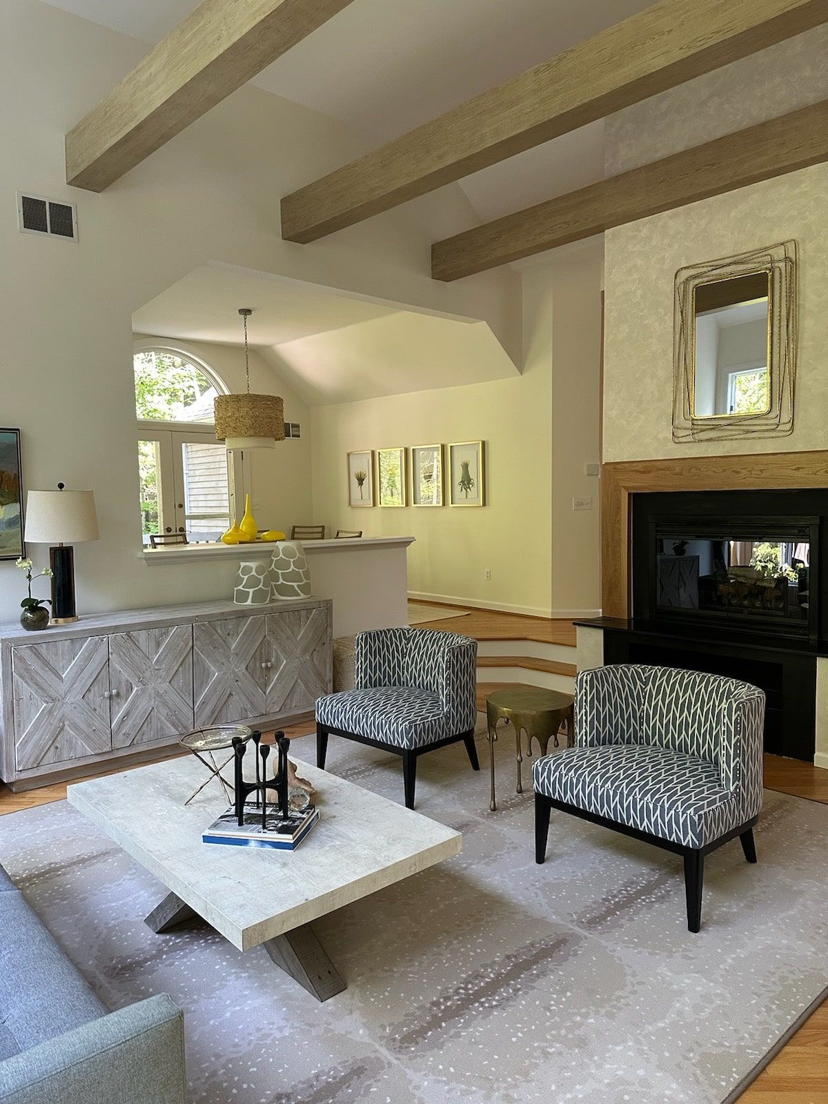 Living room with patterned armchairs, fireplace, and a decorative buffet. Beige and white color scheme.