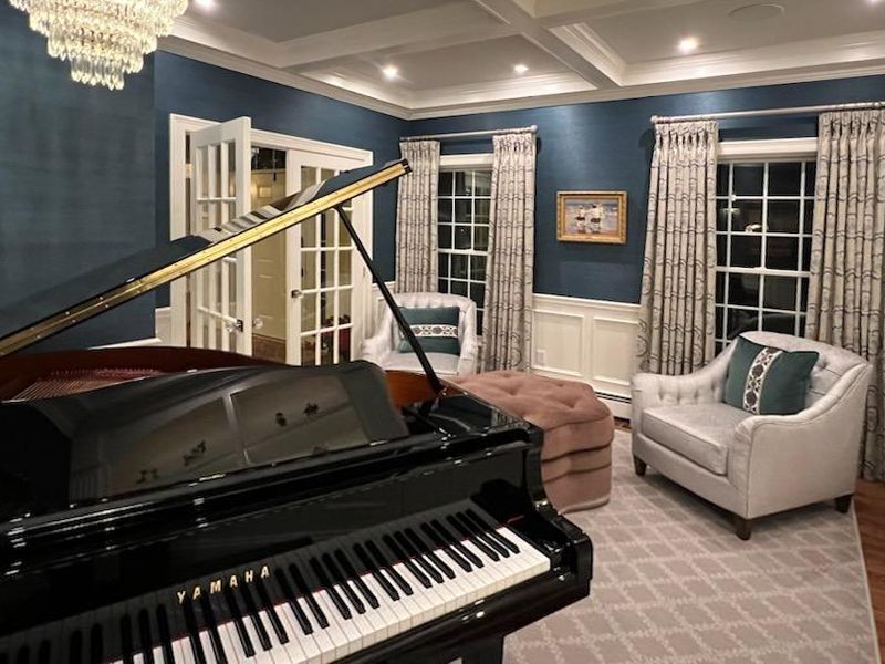 A grand piano in a music room with blue walls, white chairs, and patterned curtains.