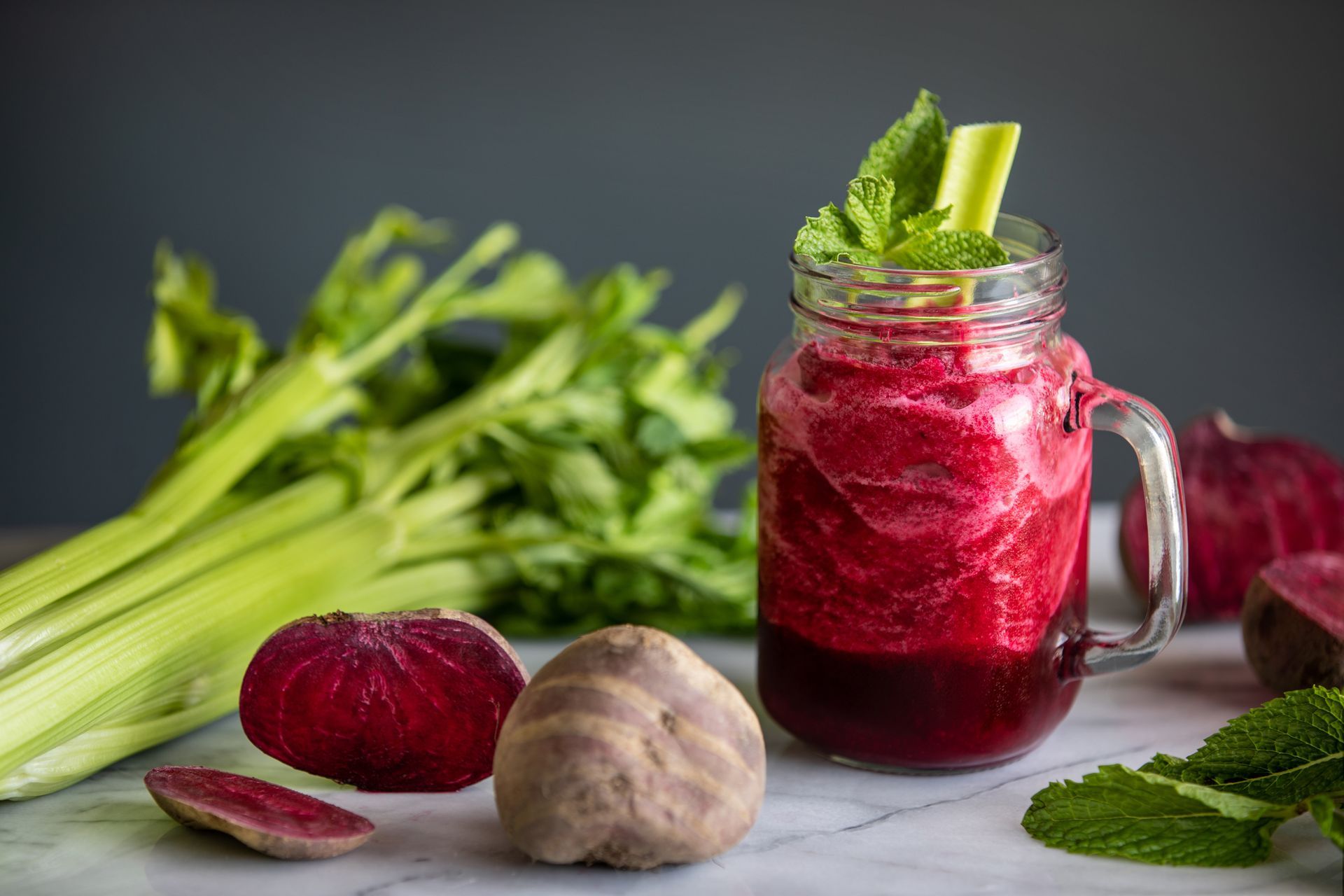 Beetroot and celery juice in a mason jar, garnished with mint and celery, with ingredients scattered around.