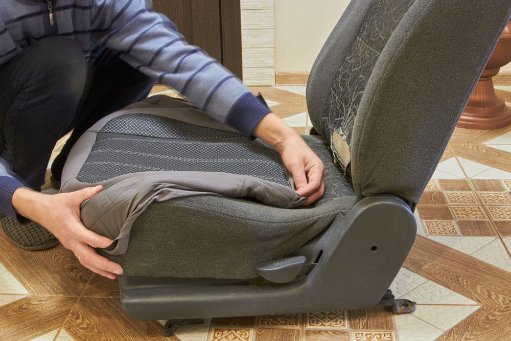 A Man Is Kneeling Down To Remove A Seat Cover From A Car Seat — Gaeta's Upholstery Blinds & Awnings in Grafton, NSW