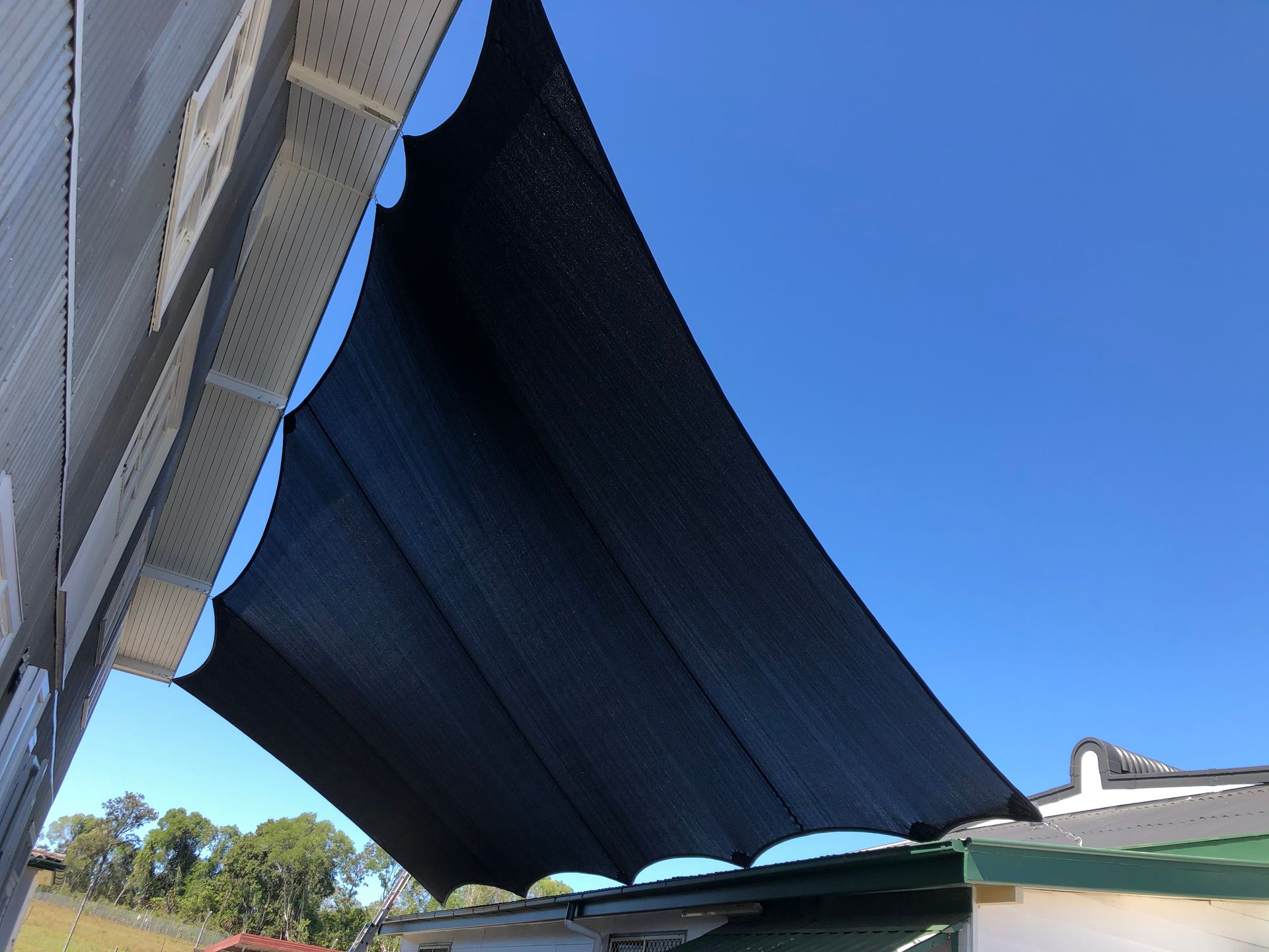 Shade Sails Are Sitting On Top Of A Lush Green Field Next To A Beach — Gaeta's Upholstery Blinds & Awnings in Glen Innes, NSW