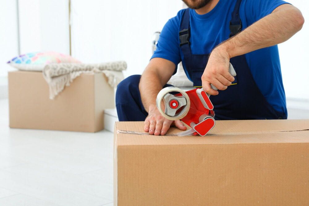 Man in Blue Overalls Seals a Cardboard Box — Cairns Mini Movers In Mount Sheridan, QLD