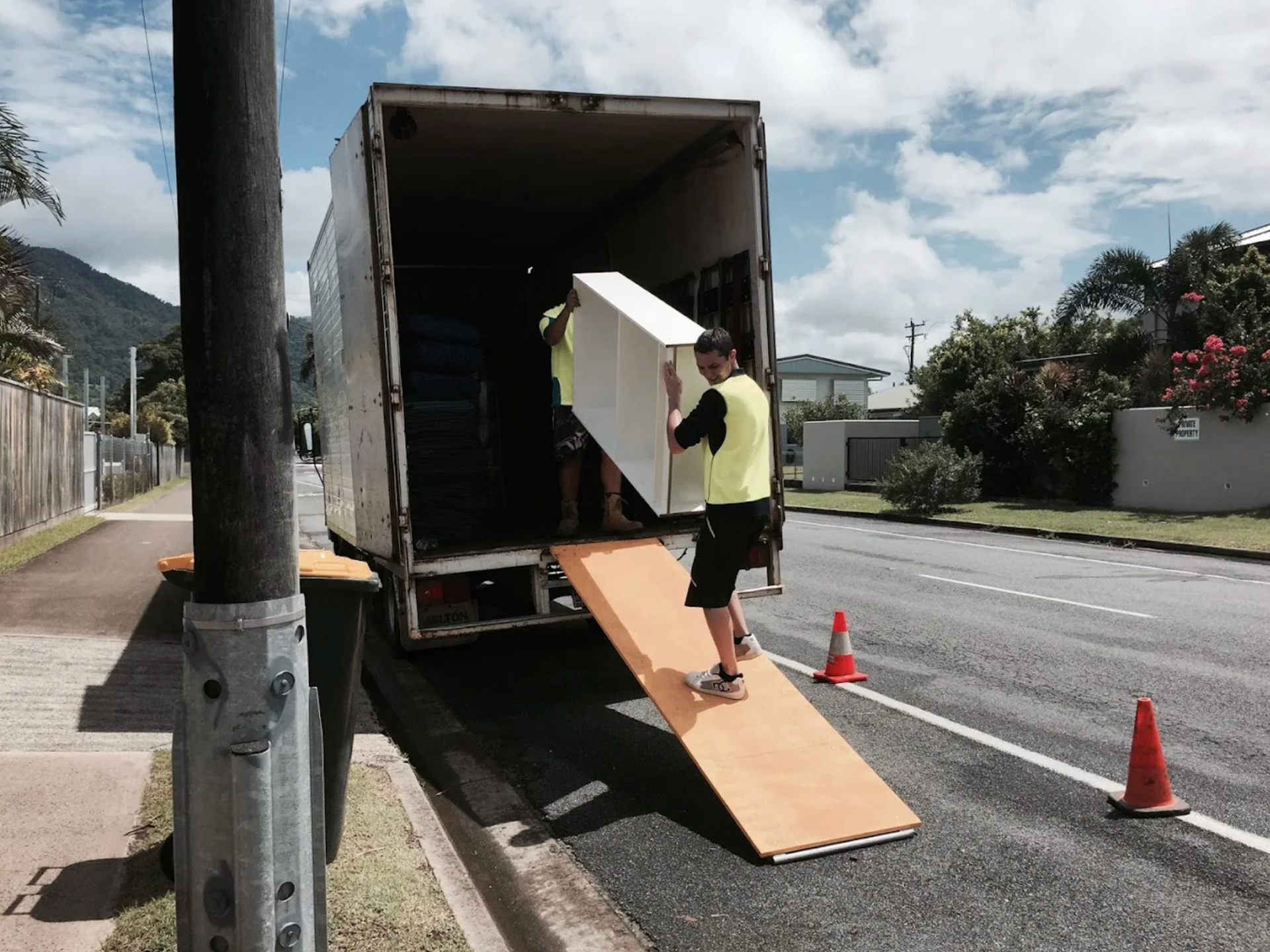 Furniture removalists unloading a large cabinet from truck at a residential home during a local move