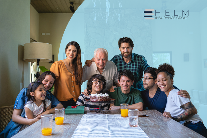 A large family is sitting around a table with a cake.