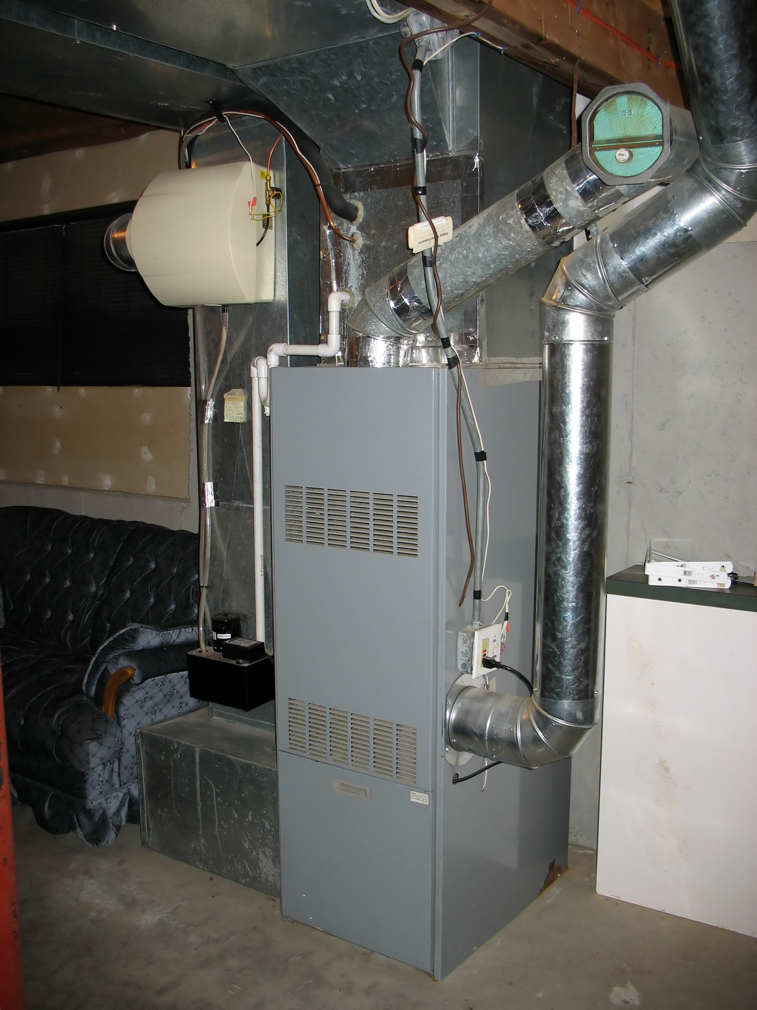 A gray furnace with ductwork in a basement. A humidifier is attached to the duct.