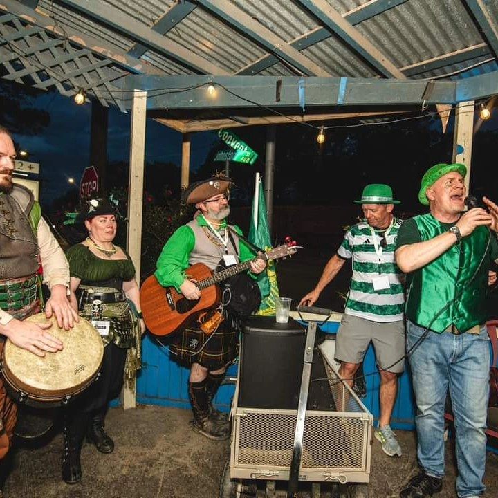 A band performs outdoors at night. Musicians in green and kilts play guitar, drums, and sing.