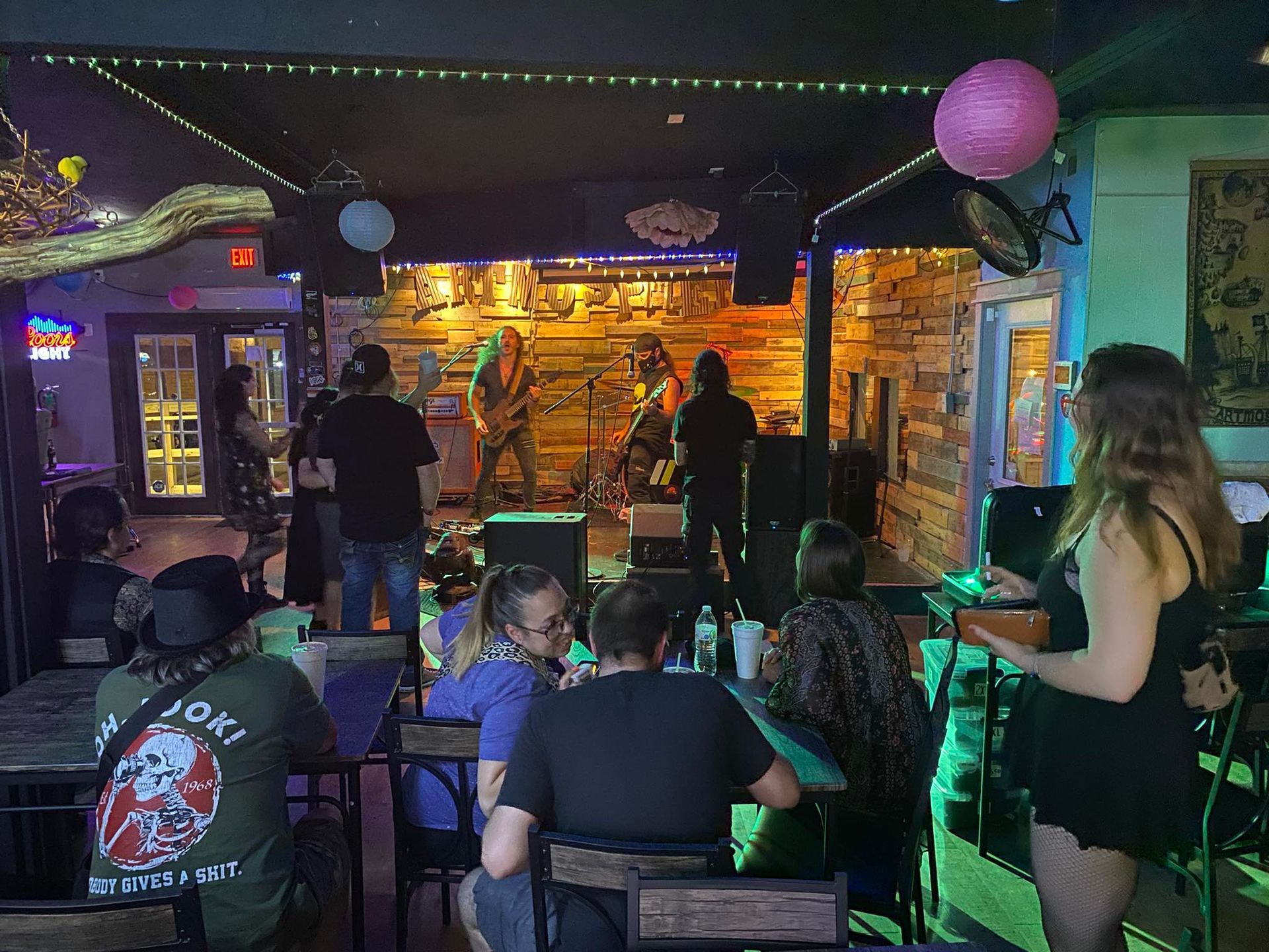 People watching a band perform in a bar. Stage lit with band members, audience at tables.
