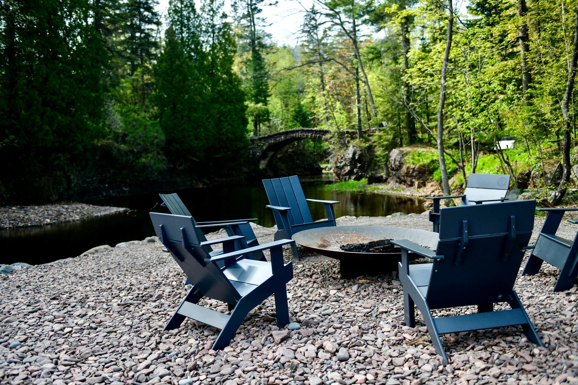 A group of chairs are sitting around a fire pit next to a river.