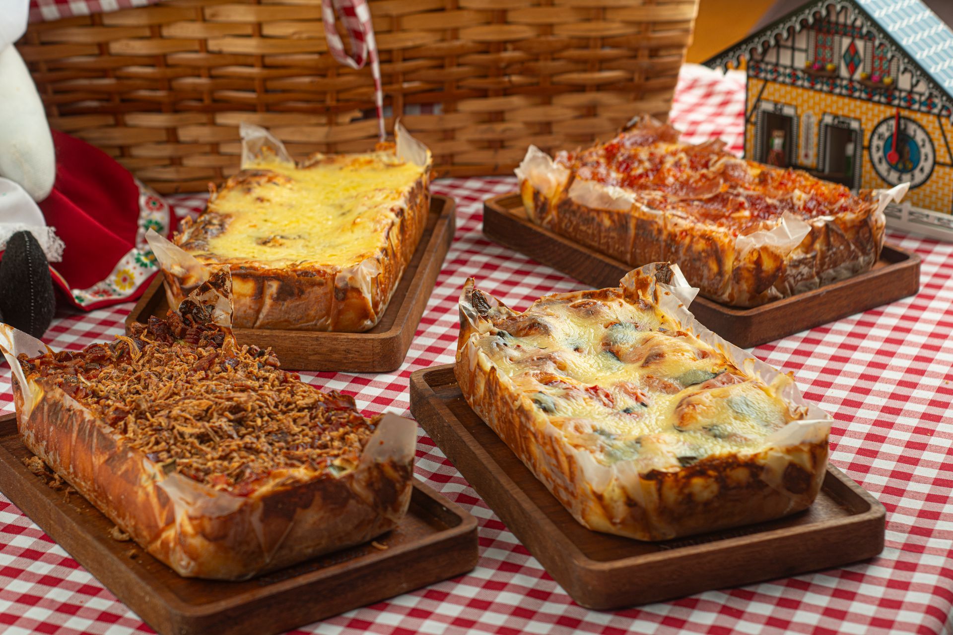 Quatro pizzas estão dispostas em bandejas de madeira sobre uma toalha de mesa xadrez.
