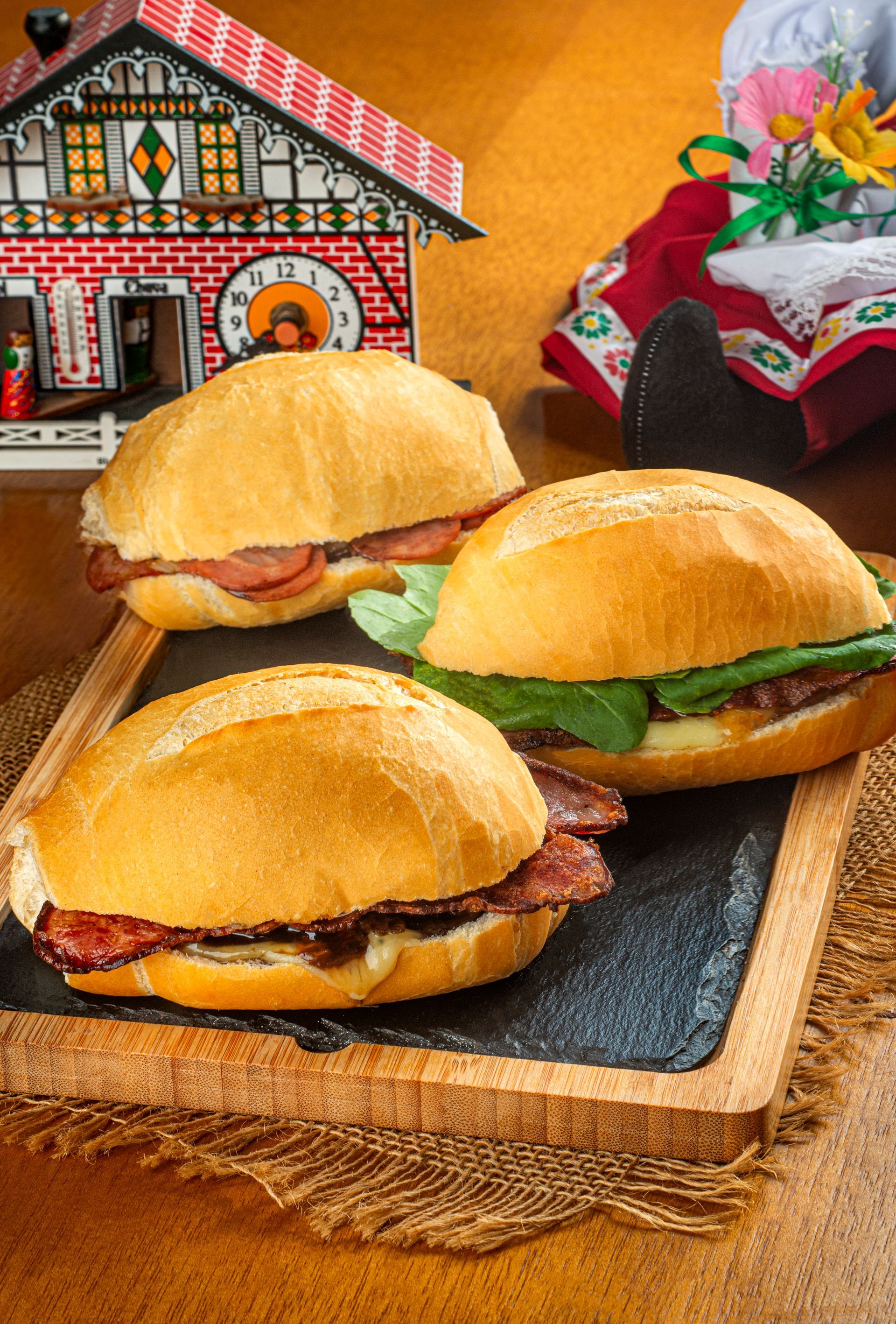 Três sanduíches estão em uma bandeja de madeira sobre uma mesa.