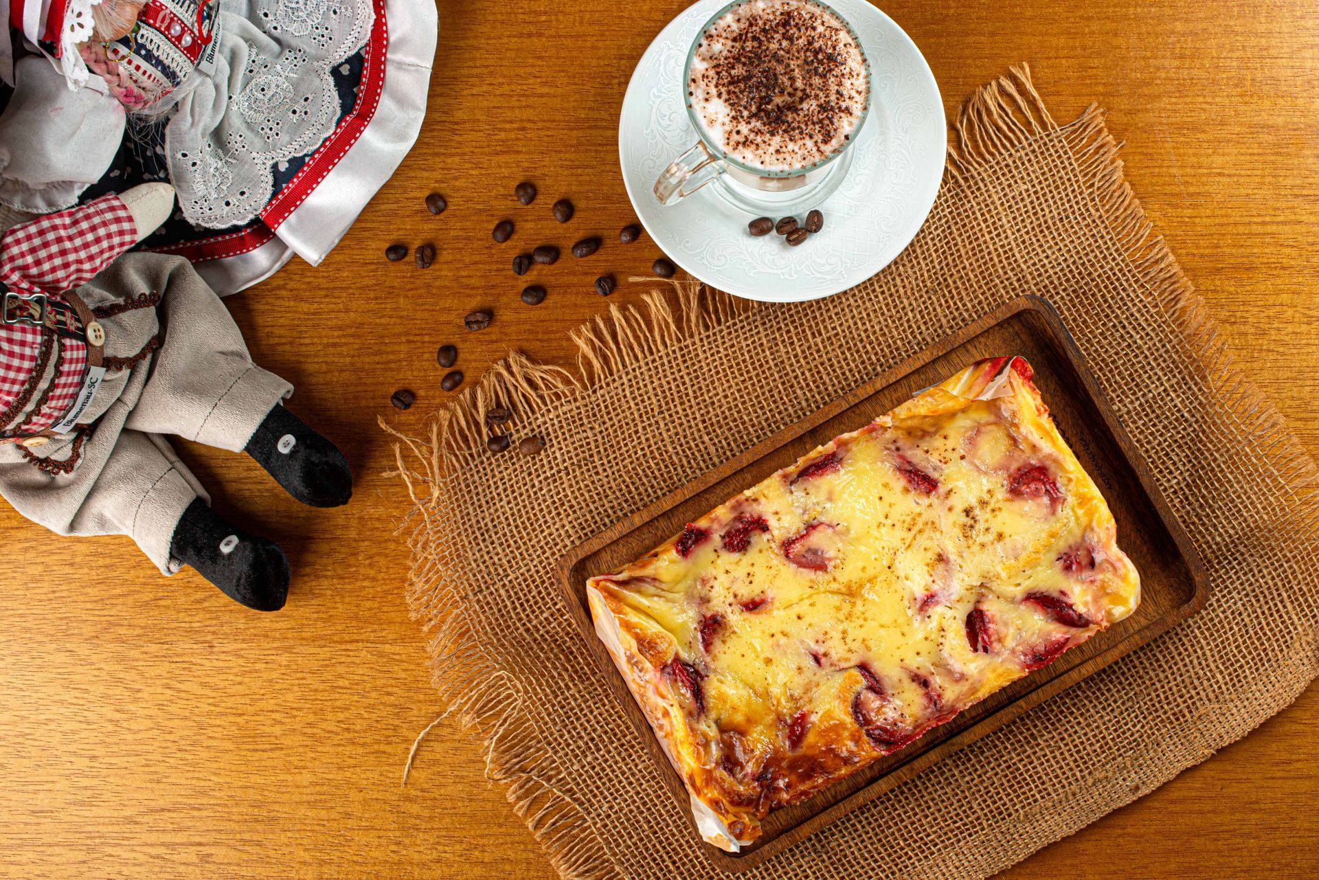 Um pedaço de cuca está sobre uma mesa de madeira ao lado de uma xícara de café.