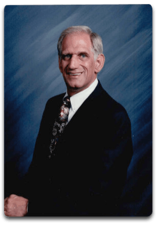 A man in a suit and tie is smiling in front of a blue background.