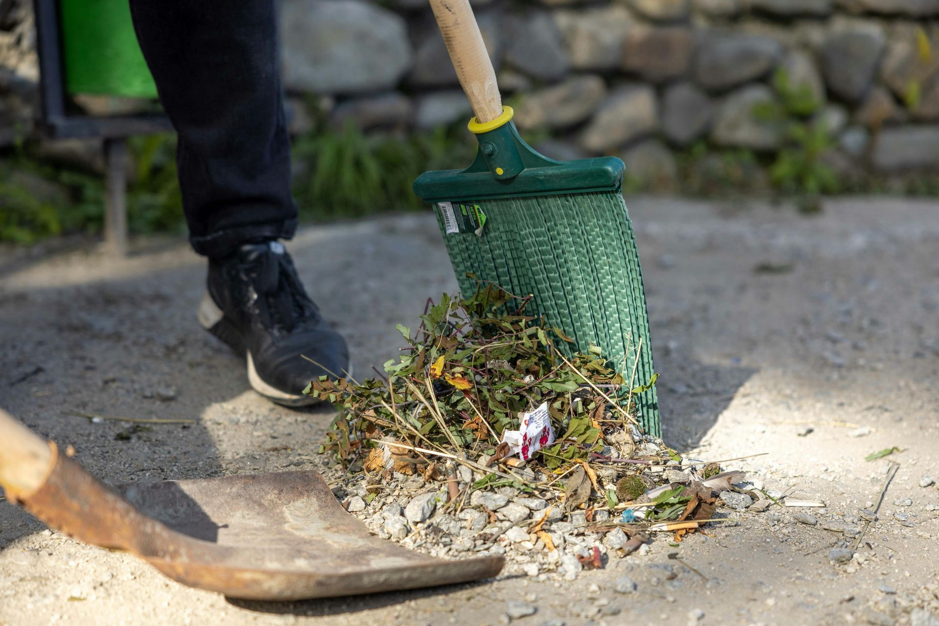 A person is sweeping the ground with a rake and shovel.