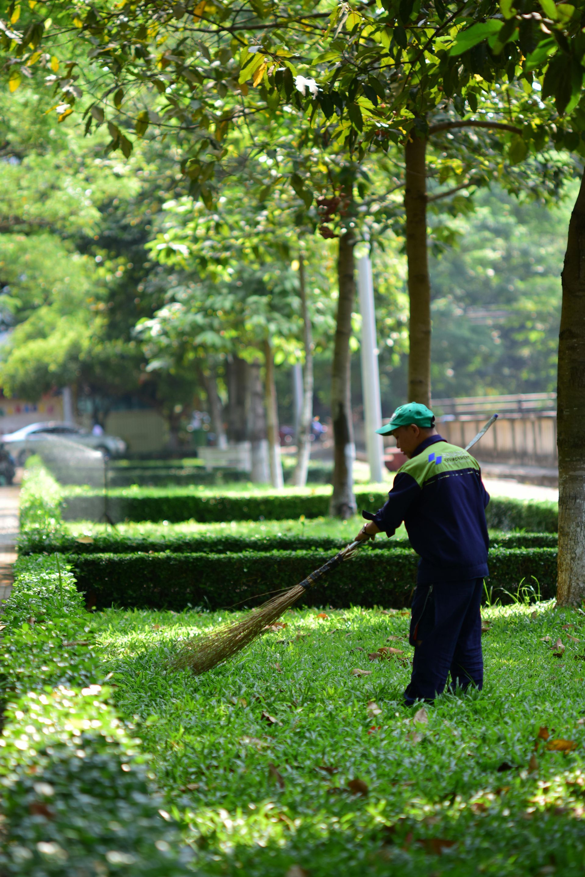 A man is sweeping the grass in a park with a broom.