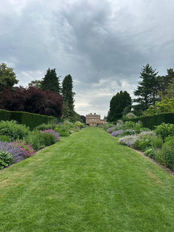 A large house is behind a lush green field of grass and flowers.