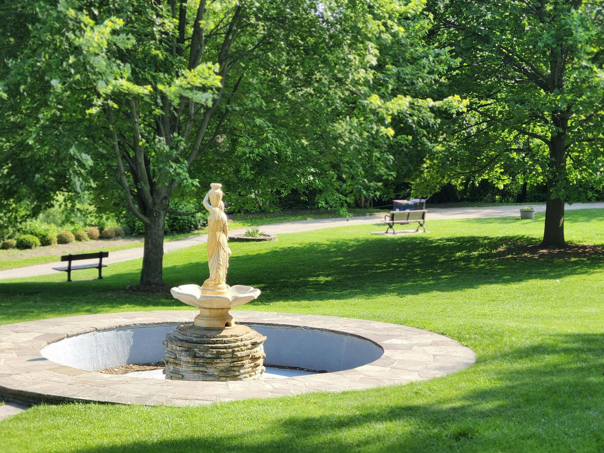A fountain in a park with a statue of a woman on top of it.