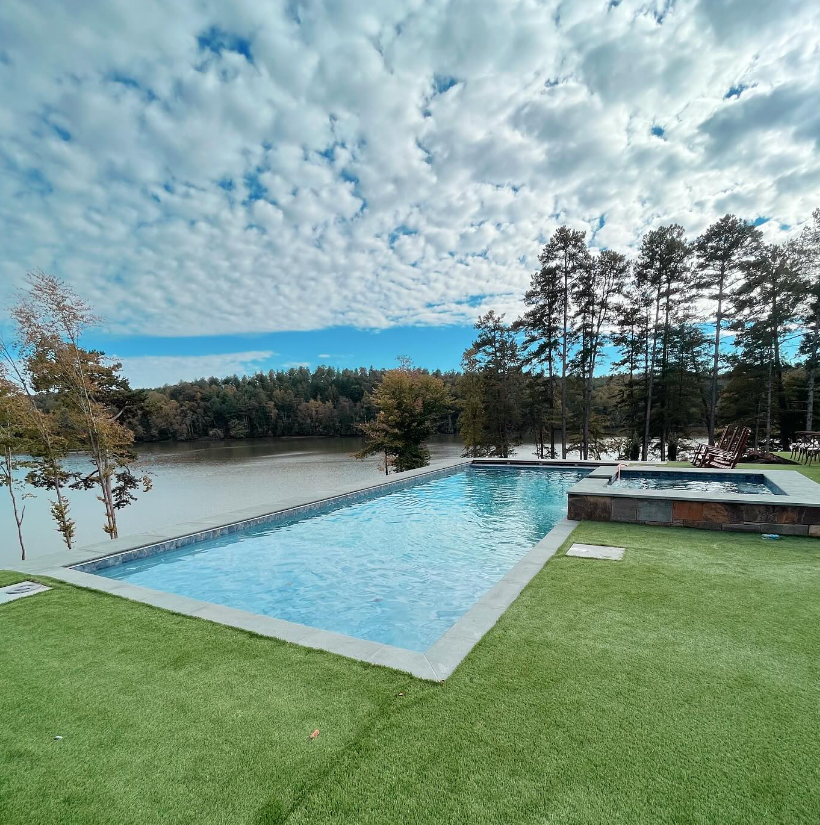 A large swimming pool with a view of a lake surrounded by trees.