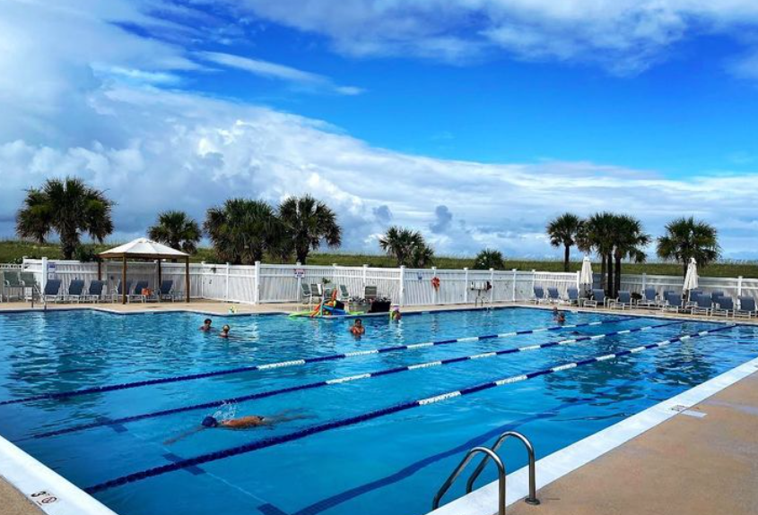 A large swimming pool with people swimming in it on a sunny day.
