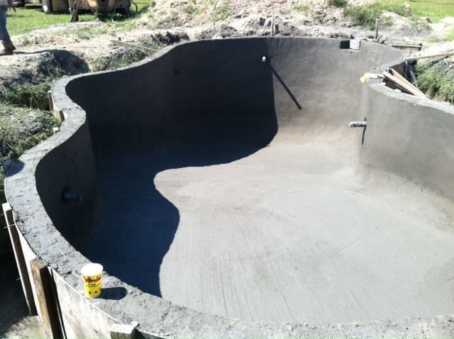 A large concrete pool is being built in a yard by Caroline Pool Plastering in Charlotte, NC