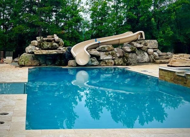 A large swimming pool with a water slide attached to it, installed by Caroline Pool Plastering in Huntsville, NC