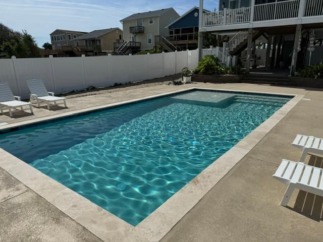 A large swimming pool is surrounded by chairs and a white fence.